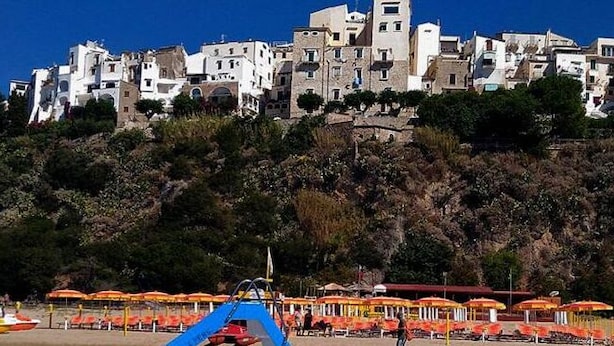 A coastal town with buildings on a hillside, beach umbrellas, and boats. - Casa Vacanza Nikita (Sperlonga)
