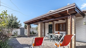 A patio with two folding chairs, a table, and a brick building with a wooden roof. - Casa Vacanza Nikita (Sperlonga)