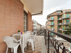 Un balcón con mesa y sillas, un muro de ladrillo y vistas a edificios cercanos.