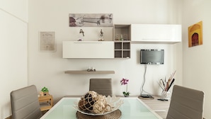 A modern living room with a glass dining table, two chairs, a sofa, a TV, and a decorative wall piece. - Casa Vacanza Scilla (Sperlonga)