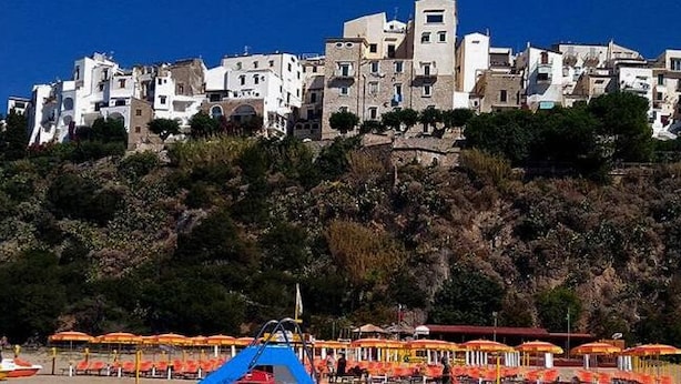 A coastal town with buildings on a hillside, beach umbrellas, and a boat. - Casa Vacanza Scilla (Sperlonga)