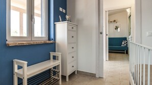 Un pasillo con pared azul, un banco blanco, un aparador blanco y un sofá verde azulado al fondo.