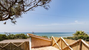 Una terraza de madera con vista al mar, una cerca de bambú y un cielo despejado.