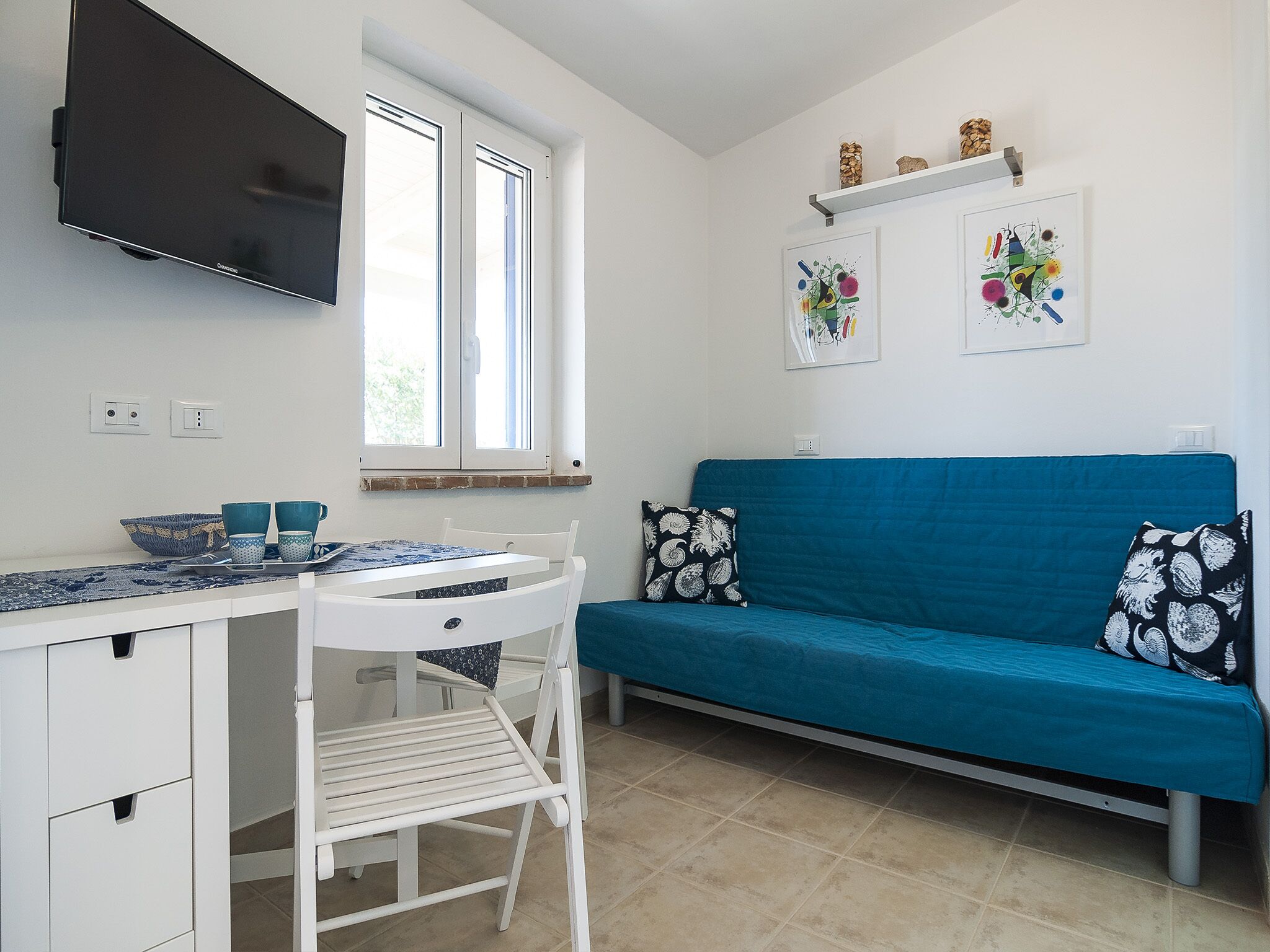 A compact kitchen with a dining area, a blue sofa, and artwork on the wall.