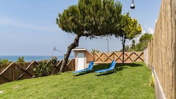 A backyard with a tree, two blue lounge chairs, a small shed, and a wooden fence.
