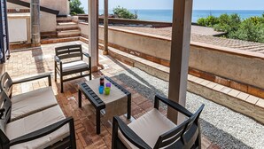 Un espacio de estar al aire libre techado con vista al mar, que cuenta con muebles de madera y una mesa con bebidas.