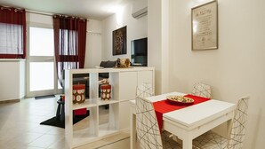 A modern dining area with a white table and chairs, a red table runner, and decorative items on the shelves. - Casa Vacanza Cariddi Loft (Sperlonga)