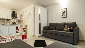 A modern living room with a grey sofa, a black rug, and a magazine on the floor. There is a kitchen area with white cabinets and a tiled backsplash. - Casa Vacanza Cariddi Loft (Sperlonga)