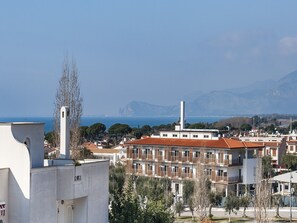A coastal cityscape with a prominent white building with a tall chimney, surrounded by residential buildings with red-tiled roofs and balconies. - Casa Vacanza Calipso (Sperlonga)
