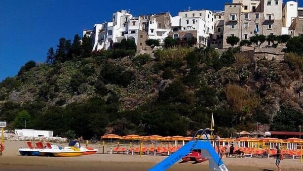 Un bote en la playa, con edificios blancos al fondo sobre una colina.