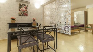 Una sala de estar moderna con una mesa de comedor de vidrio, sillas negras, una partición decorativa blanca y un cuadro de un flamenco.