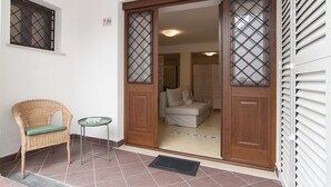 Una habitación con puerta de vidrio corredera, una silla de mimbre, una mesita pequeña y suelo de baldosas.