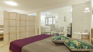 Un dormitorio con una cama, un edredón morado y almohadas con estampado tropical.