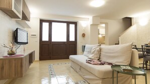Una sala de estar moderna con un sofá, una mesita, un televisor y una puerta que da a otra habitación.