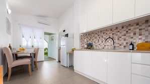 Una cocina moderna con armarios blancos, un salpicadero de azulejos y una zona de comedor con mesa y sillas.