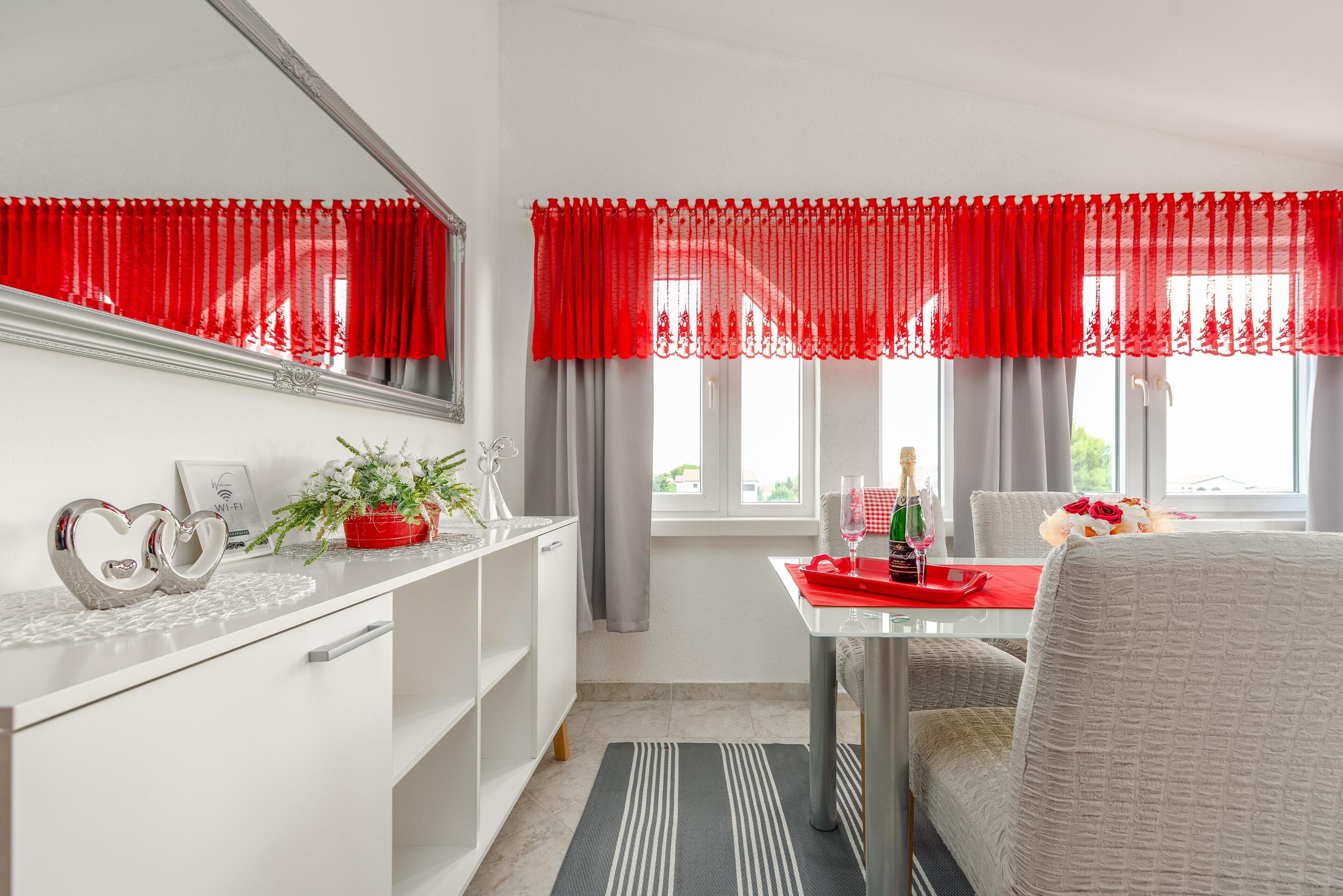A modern room with a white dresser, a mirror, a red and white striped rug, and a dining table with a red placemat.