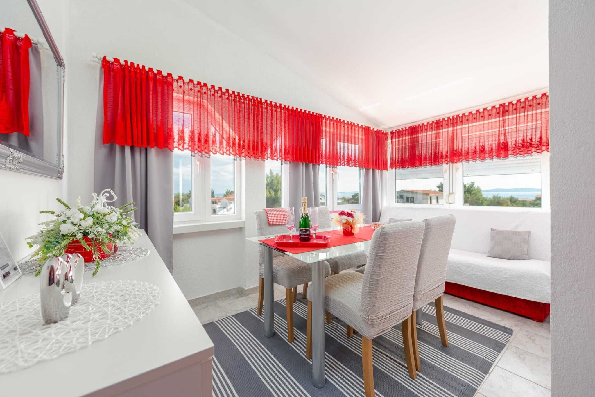 A modern dining area with a red table, white chairs, and a view of the outdoors.