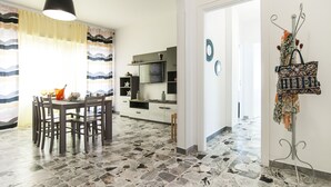 A dining area with a table and chairs, a kitchen in the background, and a hallway leading to another room. - Casa Vacanza Eolo (Sperlonga)
