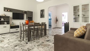 A modern living room with a dining area, featuring a stone tile floor, a brown sofa, and a dining table with chairs. - Casa Vacanza Eolo (Sperlonga)