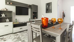 A modern kitchen with a dining table, chairs, and a TV mounted on the wall. - Casa Vacanza Eolo (Sperlonga)