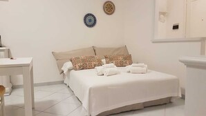 A hotel room with a bed, two pillows, a bedside table, and a small table. - Casa Vacanza Mare Verde (Sperlonga)