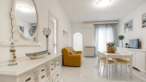 A bright, well-lit room with a white dresser, a yellow armchair, a dining table with chairs, and a large mirror. - Casa Vacanza Mare Verde (Sperlonga)