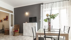A dining area with a table, chairs, a TV, and a vase with flowers. - Casa Vacanza Flora (Sperlonga)