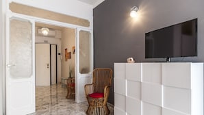 A room with a white cabinet, a television mounted on the wall, and a wicker chair with a red cushion. - Casa Vacanza Flora (Sperlonga)