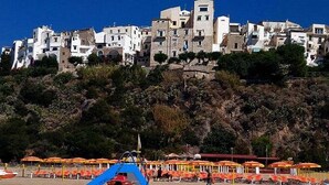 A coastal town with buildings on a hillside, beach umbrellas, and a lifeguard tower.