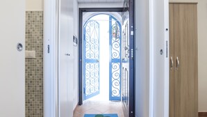 A hallway with a blue door with intricate metalwork, a wooden wardrobe, and a tiled floor.