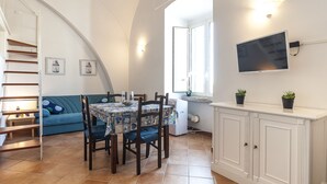 A dining area with a table and chairs, a sofa, a staircase, and a TV mounted on the wall.