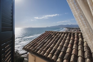 Vista sulla costa dal balcone con tetto in tegole, che si affaccia sul mare e su una catena montuosa in lontananza.