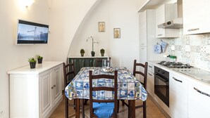 A compact kitchen with white cabinetry, a tiled backsplash, and a dining area with a table covered in a blue and white patterned tablecloth.