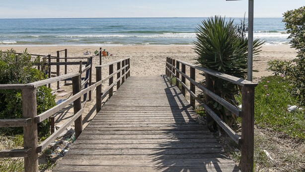 Een houten looppad dat naar een strand leidt, met een bord waarop de waterkwaliteit wordt aangegeven.