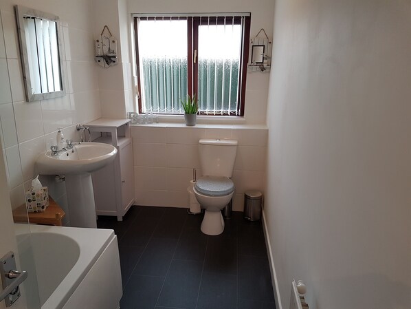 A bathroom with a bathtub, sink, toilet, and window with curtains.