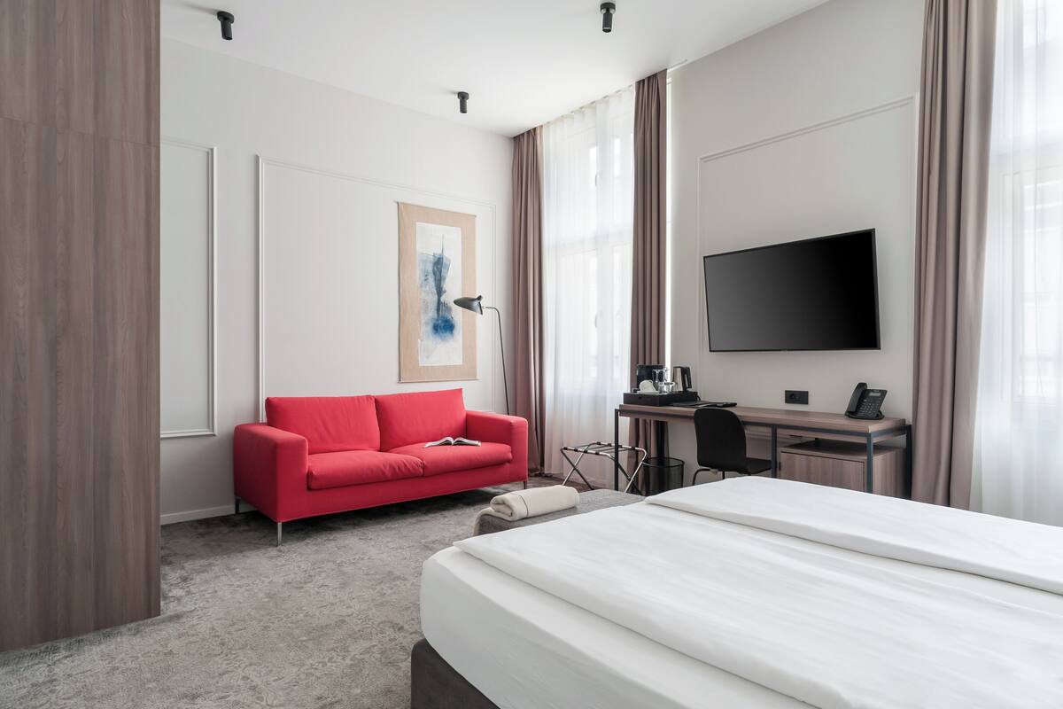 Una habitación de hotel moderna con una cama grande, un sofá rojo, un escritorio con computadora y un televisor de pantalla plana.