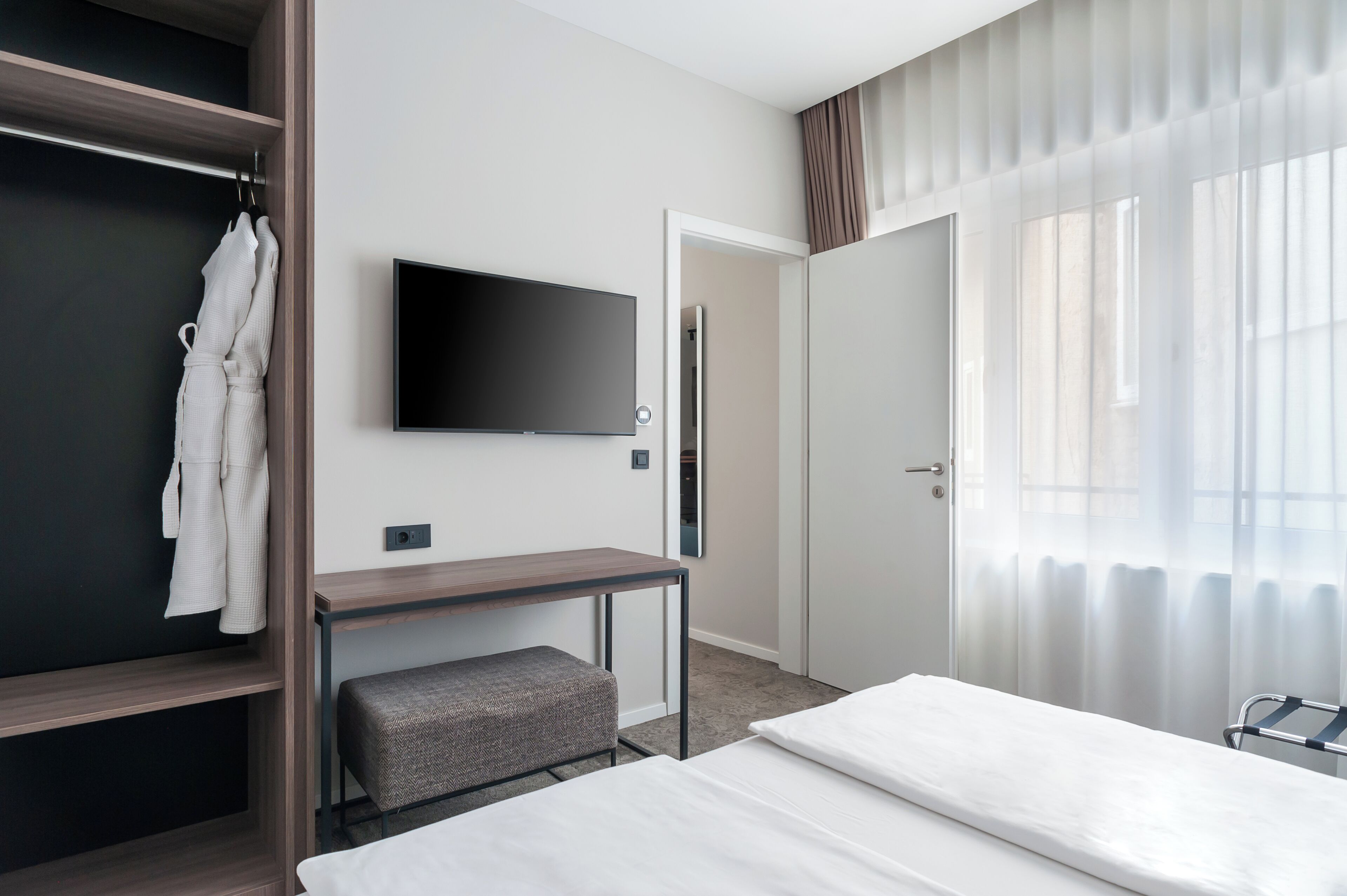 Una habitación de hotel con una cama, televisor montado en la pared, un escritorio y un armario.