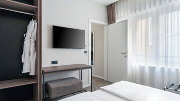 Una habitación de hotel con una cama, televisor montado en la pared, un escritorio y un armario.