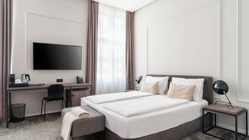 Een hotelkamer met een groot bed, een bureau met een flatscreen televisie, een stoel, een klein tafeltje met een lamp en een prullenbak.