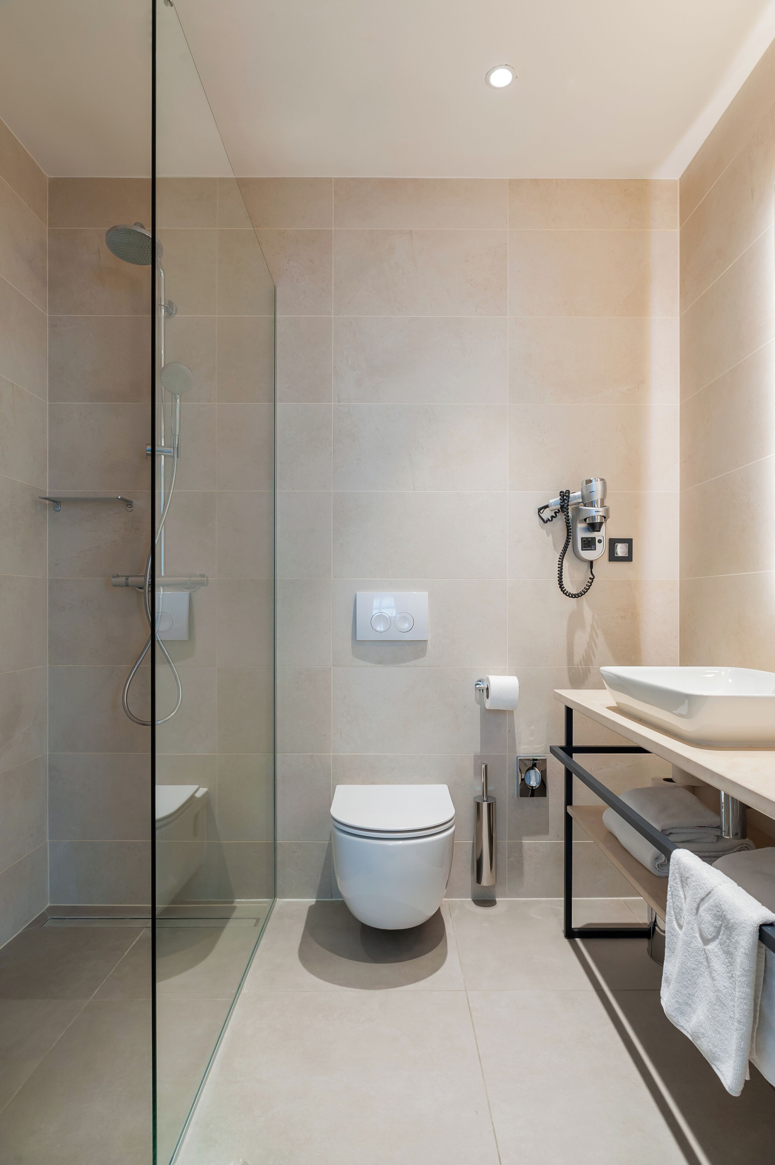 A modern bathroom with a glass-enclosed shower, a toilet, and a sink with a towel hanging on the countertop.