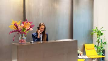 A reception desk with a vase of flowers, a phone, and a yellow chair.