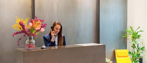 A reception desk with a vase of flowers, a phone, and a yellow chair.