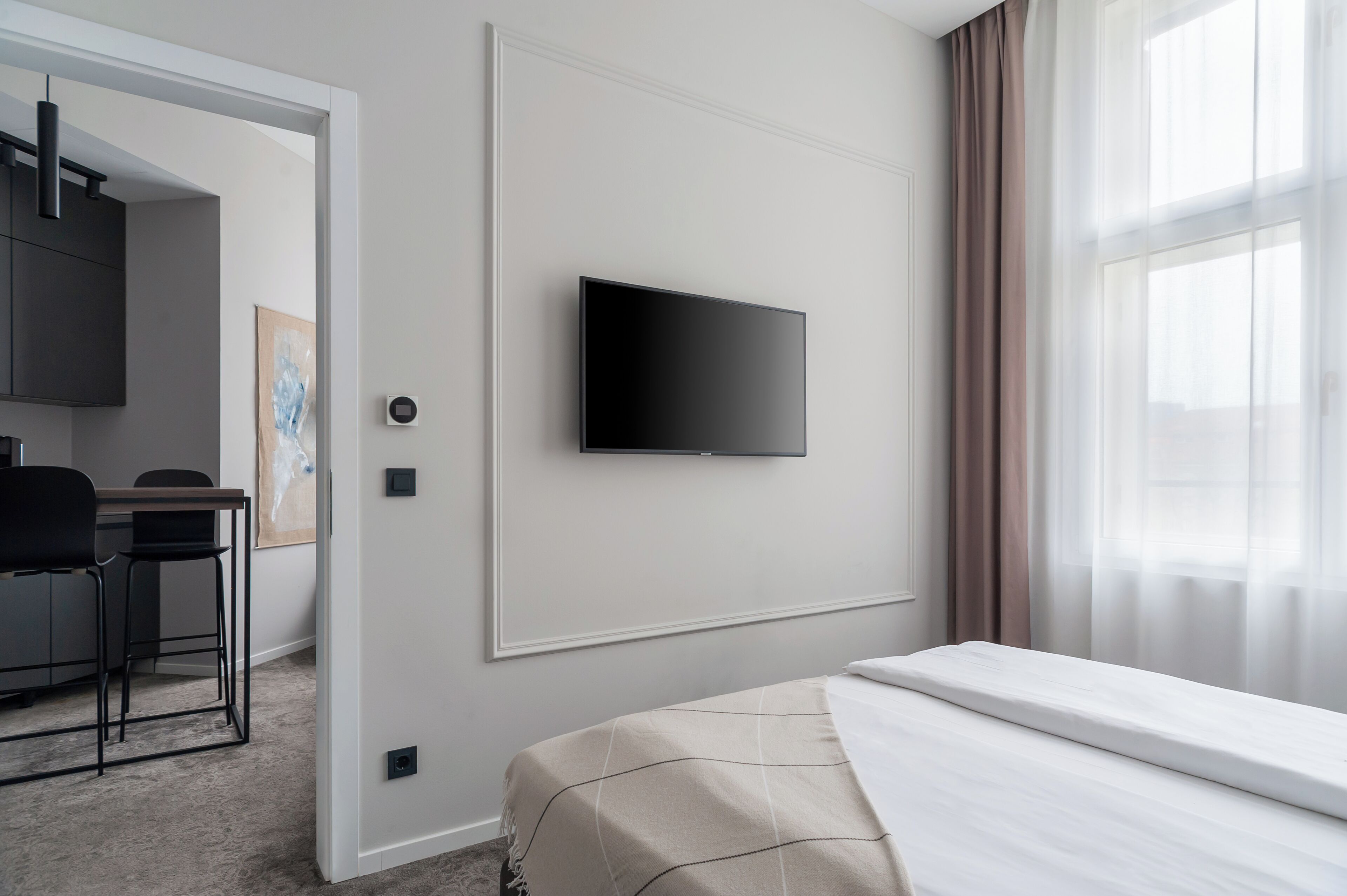 Una habitación de hotel con cama, televisor de pantalla plana en la pared, escritorio con silla y ventana con cortinas.