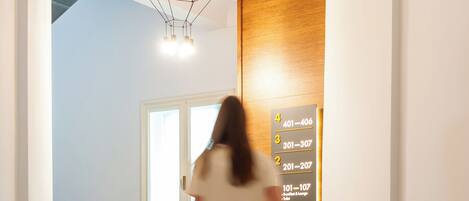 A hotel hallway with a staircase, a reception desk, and a sign indicating room numbers.