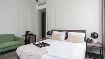 A hotel room with a large bed, a green sofa, a bedside table with a lamp, and a small desk with a phone.