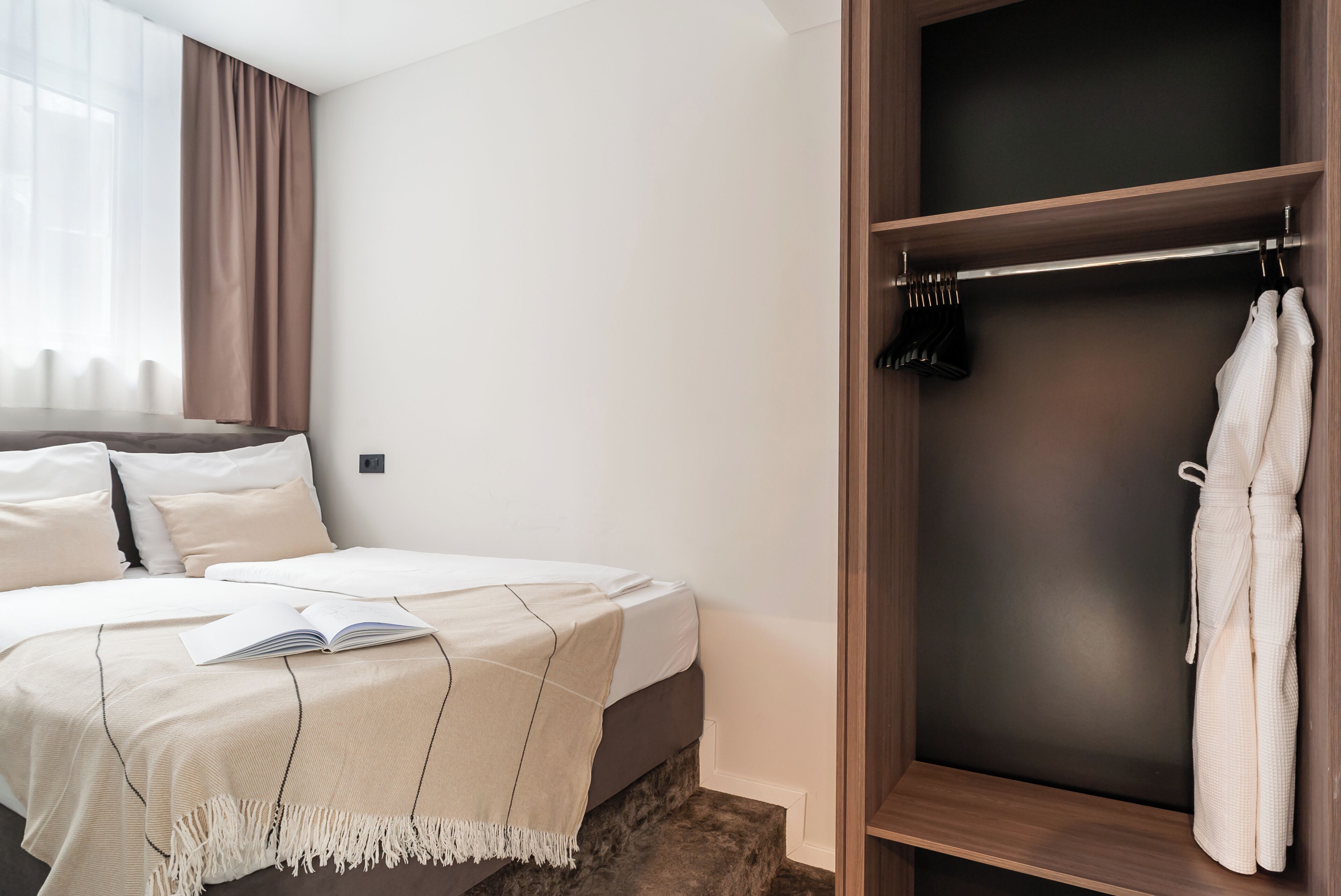 A bedroom with a bed, a bedside table with a book, a wardrobe, and a window with curtains.