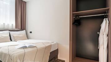 Un dormitorio con una cama, una mesita de noche con un libro, un armario y una ventana con cortinas.