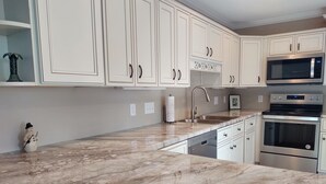 Una cocina moderna con armarios blancos, encimera de mármol, electrodomésticos de acero inoxidable y un adorno navideño con forma de muñeco de nieve.