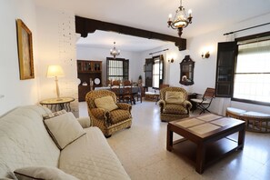 Una sala de estar con sof á, sillones, una mesa de centro, una mesa de comedor con sillas, una araña y un ventanal grande.