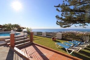 Eine Terrasse mit Pool, Meerblick und Liegestühlen.
